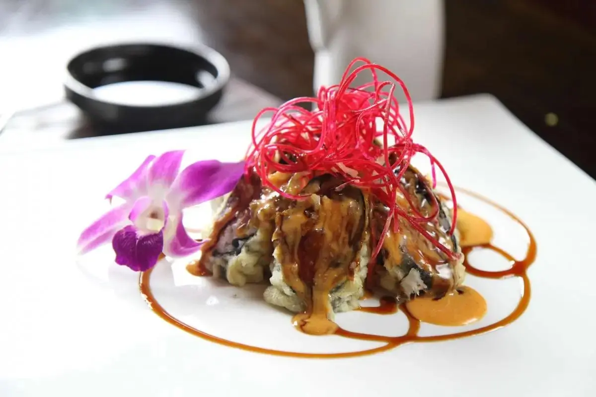 Oriental-Palace-Chinese-Restaurant-Mini-Volcano-Roll-Castaic Sushi roll with drizzled sauces and red garnish, paired with orchid, at Oriental Palace, a Asian Restaurant in Lawnside
